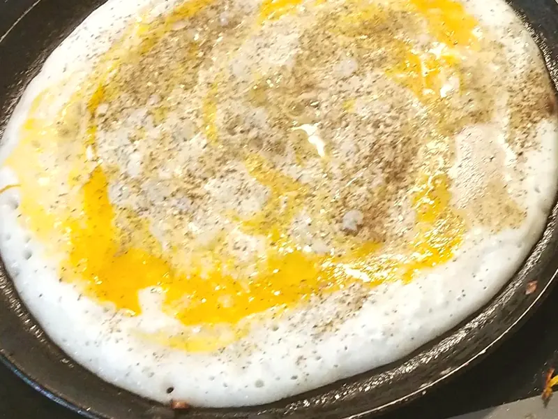 An egg dosa cooking on the tawa, egg spread across the batter