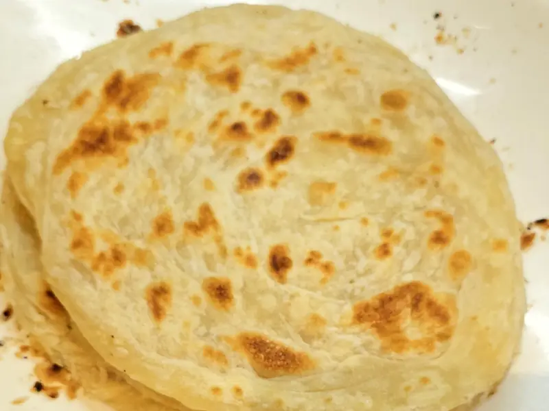 A stack of parotta, flaky layered flatbread, on a white plate