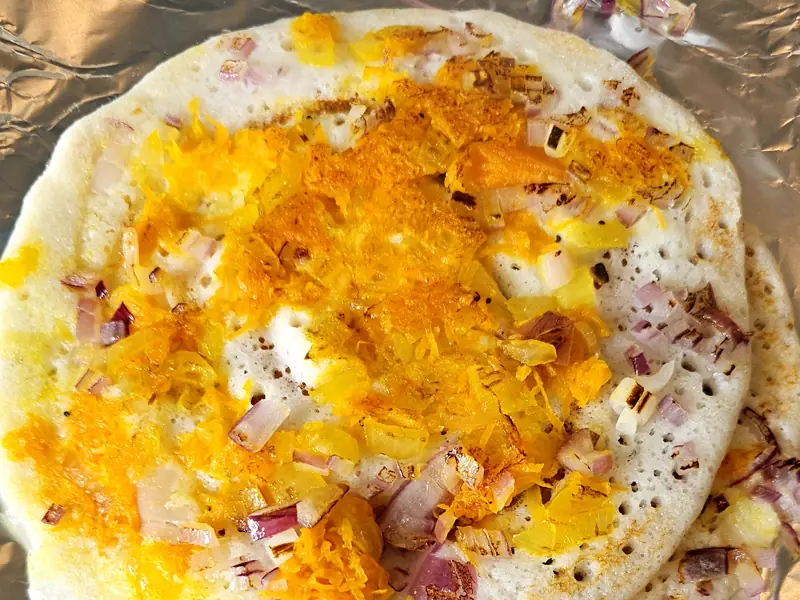 An uttapam topped with grated carrot and chopped red onion