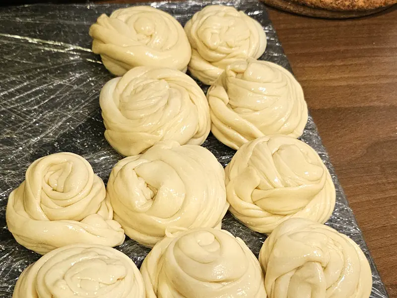 Coils of parotta dough resting on a board, a rolling pin behind them
